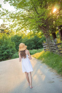 Sarı yaz şapka yürüyüş ile beyaz elbiseli sevimli genç kız. Tatil konsepti