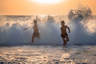 Arkalarında dalga sıçrayan iki çocuk denizden kaçıyor..