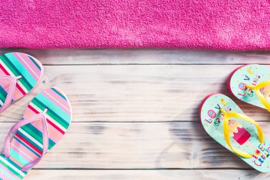 Üst tarafında pembe havlu ile beyaz ahşap arka plan üzerinde renkli parmak arası terlik.