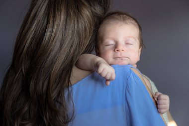 Yeni doğan bebeğini omzuna tutan genç anne.