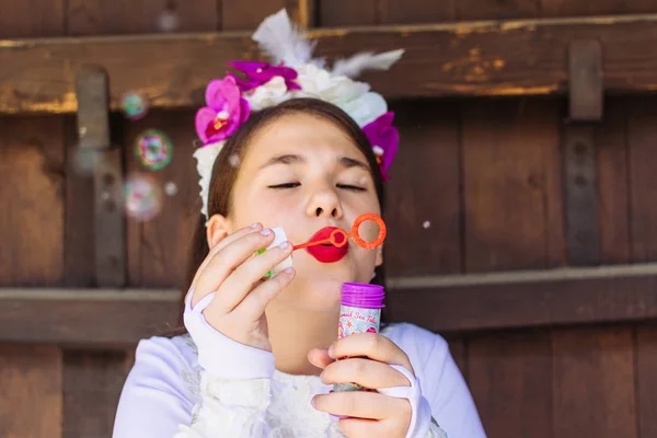 Bonito, menina com cabelo florido acessório decorativo, soprando bolhas de sabão . — Fotografia de Stock