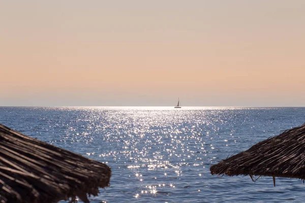 Meer mit Segelboot in der Ferne auf dem Meer mit Strohschirmen vor — Stockfoto