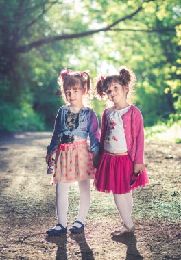 İki küçük kız, domuz kuyruklu kız kardeşler bir şeye bakıyor, el ele tutuşuyor..