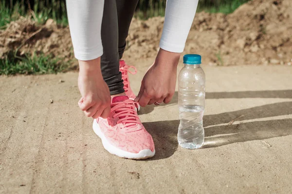 Girl tying shoelaces on her running sneakers. Water bottle next to her — Stock Photo, Image