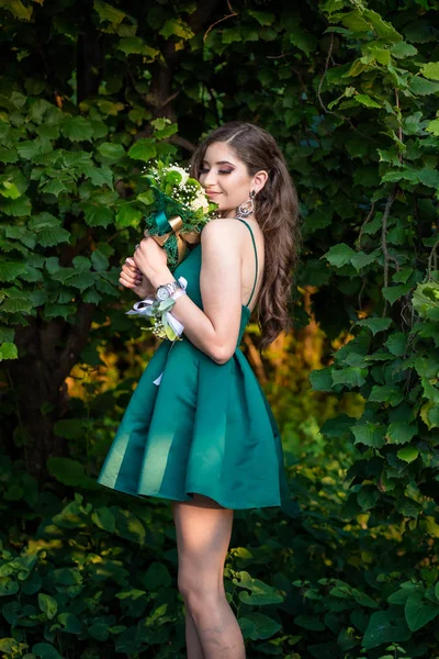 緑の壁の前にバラの花束を保持する緑のドレスのブルネットの女の子. — ストック写真