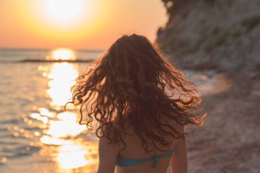 Gün batımında güzel bir kızın yakın çekim portresi. Uzun, esmer kıvırcık saç.