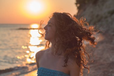 Gün batımında güzel bir kızın yakın çekim portresi. Uzun, esmer kıvırcık saç.