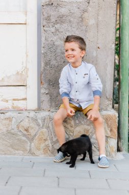 Evcil hayvanını tutan çocuk, sokakta küçük siyah köpek yavrusu.