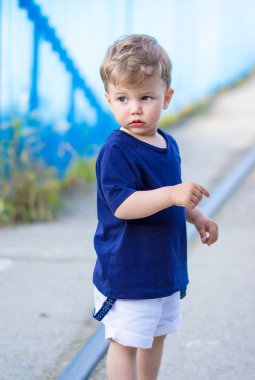 Mavi t-shirt sevimli küçük sarışın çocuk, ayakta, şaşkın görünümlü