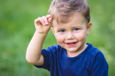 Mavi tişörtlü çocuk parkta otururken eliyle bir şeyler gösteriyor..