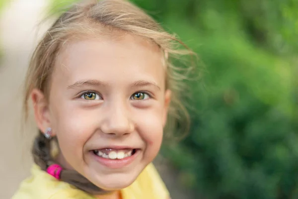背景に緑の草と黄色い緑色の目を持つブロンドの小さな女の子. — ストック写真
