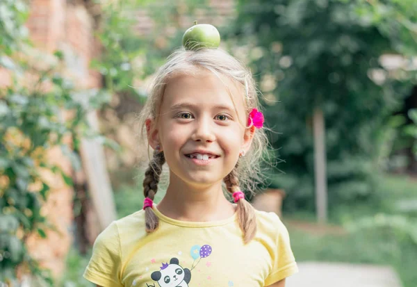 Linda niña rubia con manzana verde en la cabeza. Alimentación saludable —  Fotos de Stock