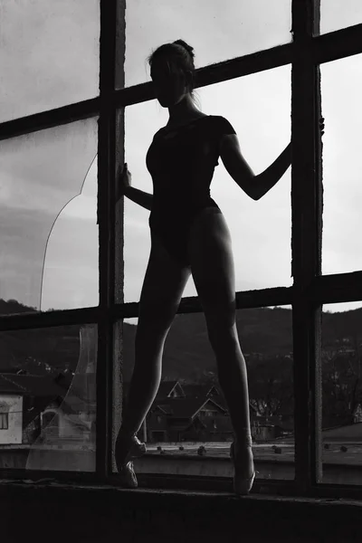 Black and white photo of ballerina in the window frame in an old building — Stock Photo, Image