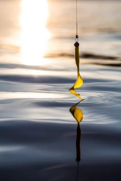 Fish hook with yellow silicone bait touching the surface of the water.