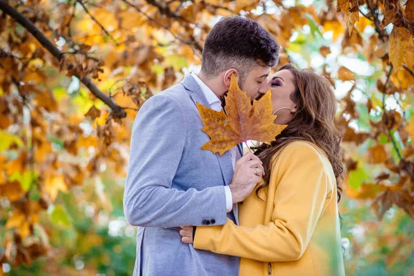 Foto al aire libre, hermosa pareja joven besándose detrás de la hoja de roble amarillo . —  Fotos de Stock