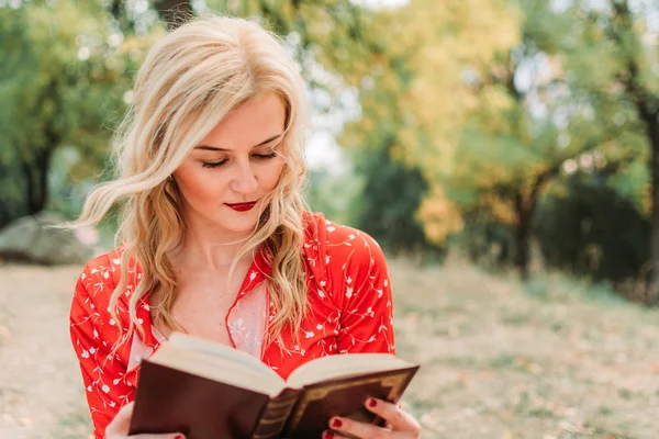 Schöne Dame in rotem Hemd sitzt im Park und liest ein Buch — Stockfoto