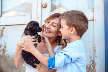 Sevimli sarışın çocuk ve annesi sokakta evcil hayvanını tutan, küçük siyah köpek yavrusu.