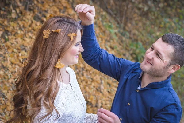 Um casal a divertir-se lá fora. Namorado jogando folhas em sua cabeça namoradas — Fotografia de Stock
