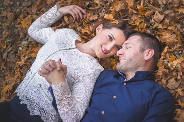 Pareja tendida en el suelo cubierta de hojas amarillas de otoño . — Foto de Stock