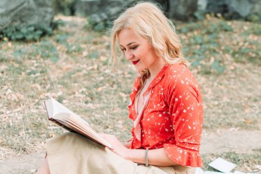 Güzel bayan kırmızı gömlekli parkta oturup kitap okuyor.