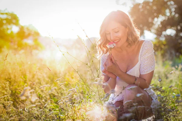 Belle dame blonde en robe blanche avec rose dans le jardin. Éclair de soleil . — Photo