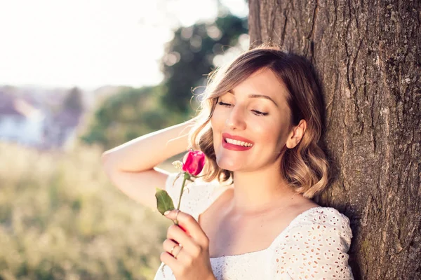 Hermosa dama rubia en vestido blanco con rosa en el jardín — Foto de Stock