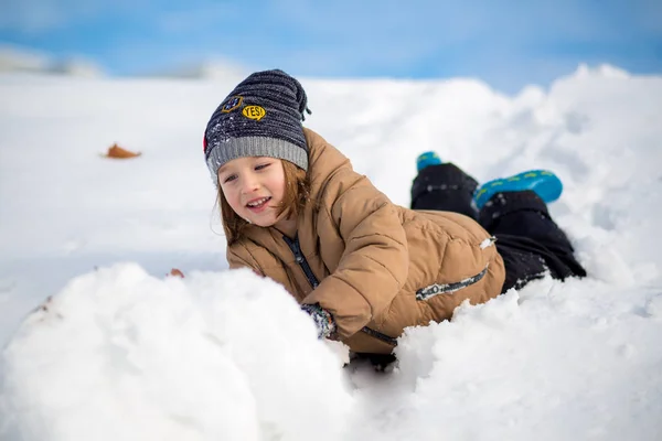 Pojke ha roligt, spela utanför, omgiven av snö. — Stockfoto