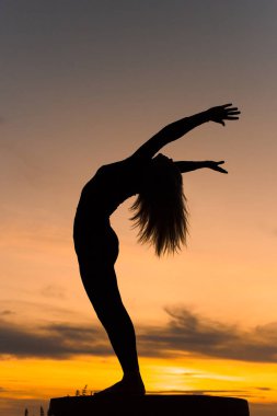 Siluet kadın gün batımında yoga antrenmanı yapıyor. Duran Arka Büküm Pozu.