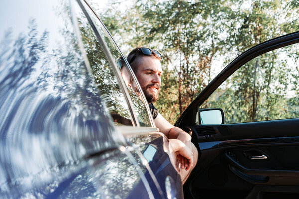 Милый бородатый мужчина, сидящий перед машиной, открытая дверь
.
