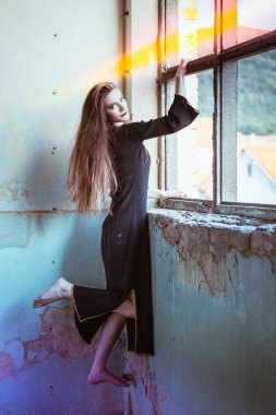 Cadı gibi giyinmiş, çılgın bakışlı, pencerede asılı bir kız. Cadılar Bayramı konsepti