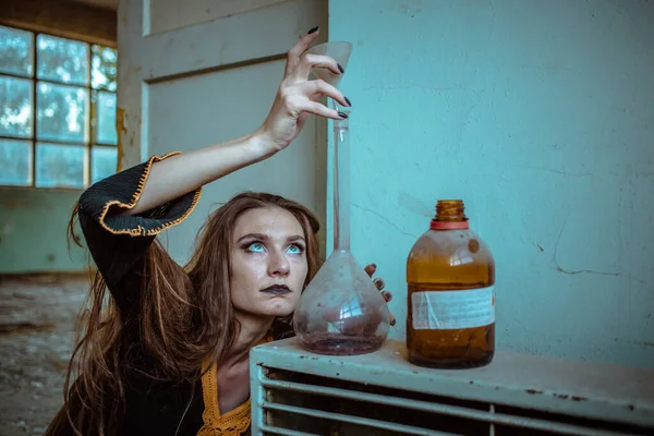 Chica vestida de bruja, mirada loca, usando cristalería de laboratorio para hacer veneno . — Foto de Stock
