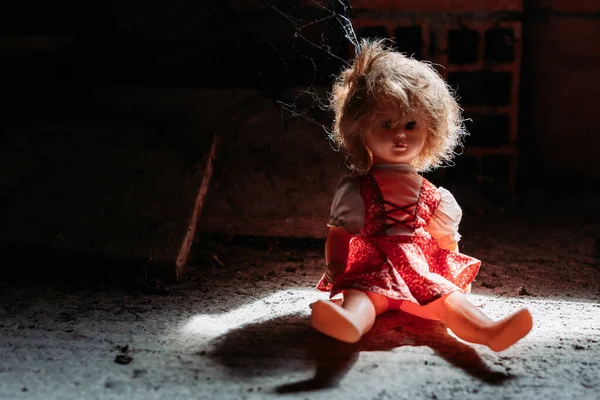 Old doll sitting on dirty ground. Scary look, Halloween concept — Stock Photo, Image