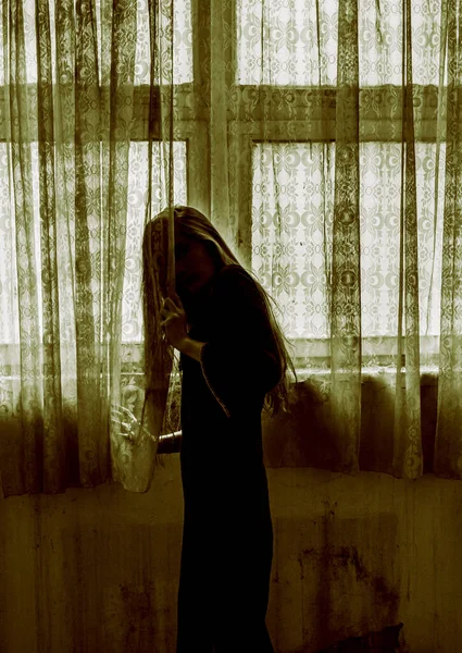 Girl dressed as witch, standing behind the curtain, scary scene.