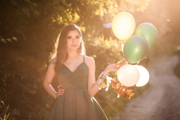 Chica en vestido verde glamoroso caminando por el camino sosteniendo globos de colores . — Foto de Stock