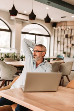 Orta yaşlı bir adam kafede dizüstü bilgisayarda çalışıyor, el ele tutuşuyor.