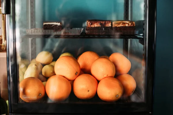 Fresh oranges and cakes inside glass display fridge in cafe restaurant