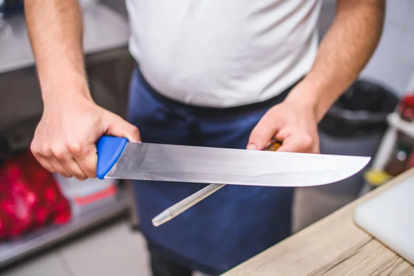 Male chef sharpening steel knife on the sharpener. Getting ready for work