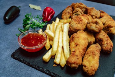 Tabakta altın tavuk nugget ve yanında patates kızartması ve sebze. Yan görünüm