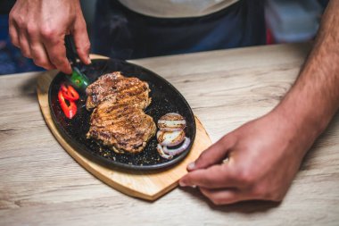 Şefin ellerinin yakın plan fotoğrafı. Biftek, kırmızı biber ve soğanlı ızgara hazırlıyor.