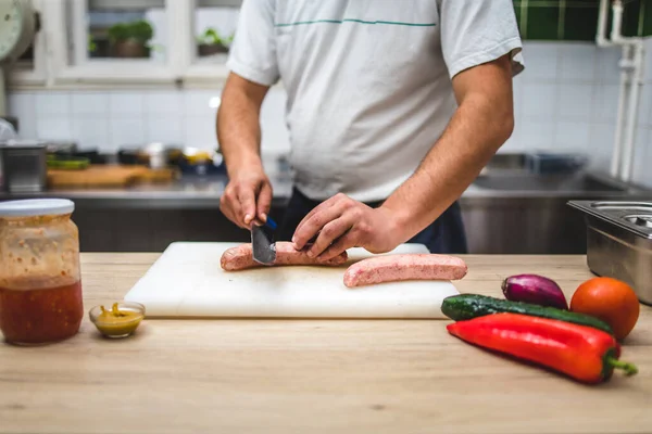 男性シェフは生肉ソーセージを野菜と一緒にボード上で切断します 食事の準備 レストラン — ストック写真