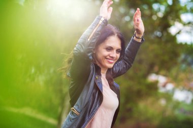 Siyah deri ceketli güzel, orta yaşlı bir kadın hayattan zevk alırken gülümsüyor, elleri havada. İlkbahar, açık hava