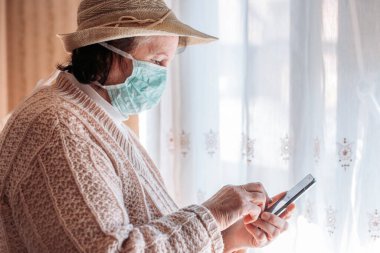 Tecritteki yaşlı kadın tıbbi maske takıyor, cep telefonu kullanıyor. Karantina hayatı