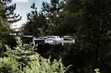 Arka planda ağaçlarla havada süzülen bir dron. Açık hava fotoğrafı