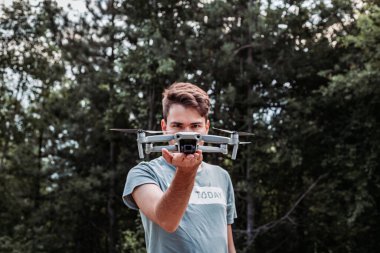 Genç adam elinde drone 'u gözünün önünde tutuyor. Açık hava fotoğrafı.
