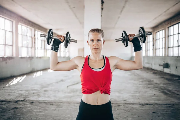 Fit blond woman weight lifting in red sportswear. Training, active lifestyle. Arms workout