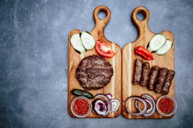 Dilimlenmiş salatalıklı, domatesli, soğanlı, kırmızı biberli, ızgara etli, Türk hamburgerli ahşap mutfak tahtası.