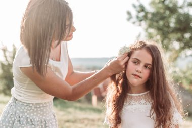 Genç anne kızının saçına beyaz çiçekler takıyor. Anne kız ilişkisi