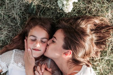 Anne ve kızı çimlerin üzerinde uzanıp öpüşüyor ve birlikte vakit geçiriyorlar.
