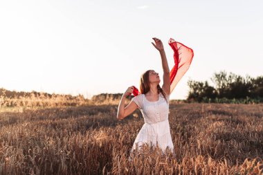 Açık havada, beyaz elbiseli kızıl bir kızın kırmızı bir eşarbı havada çırpınırken fotoğrafı..