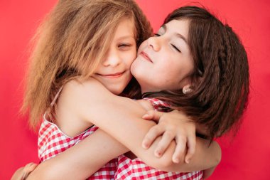 İki küçük kız kardeş, sıkıca sarılıyorlar, mutlu görünüyorlar. Pembe arka planda izole edilmiş